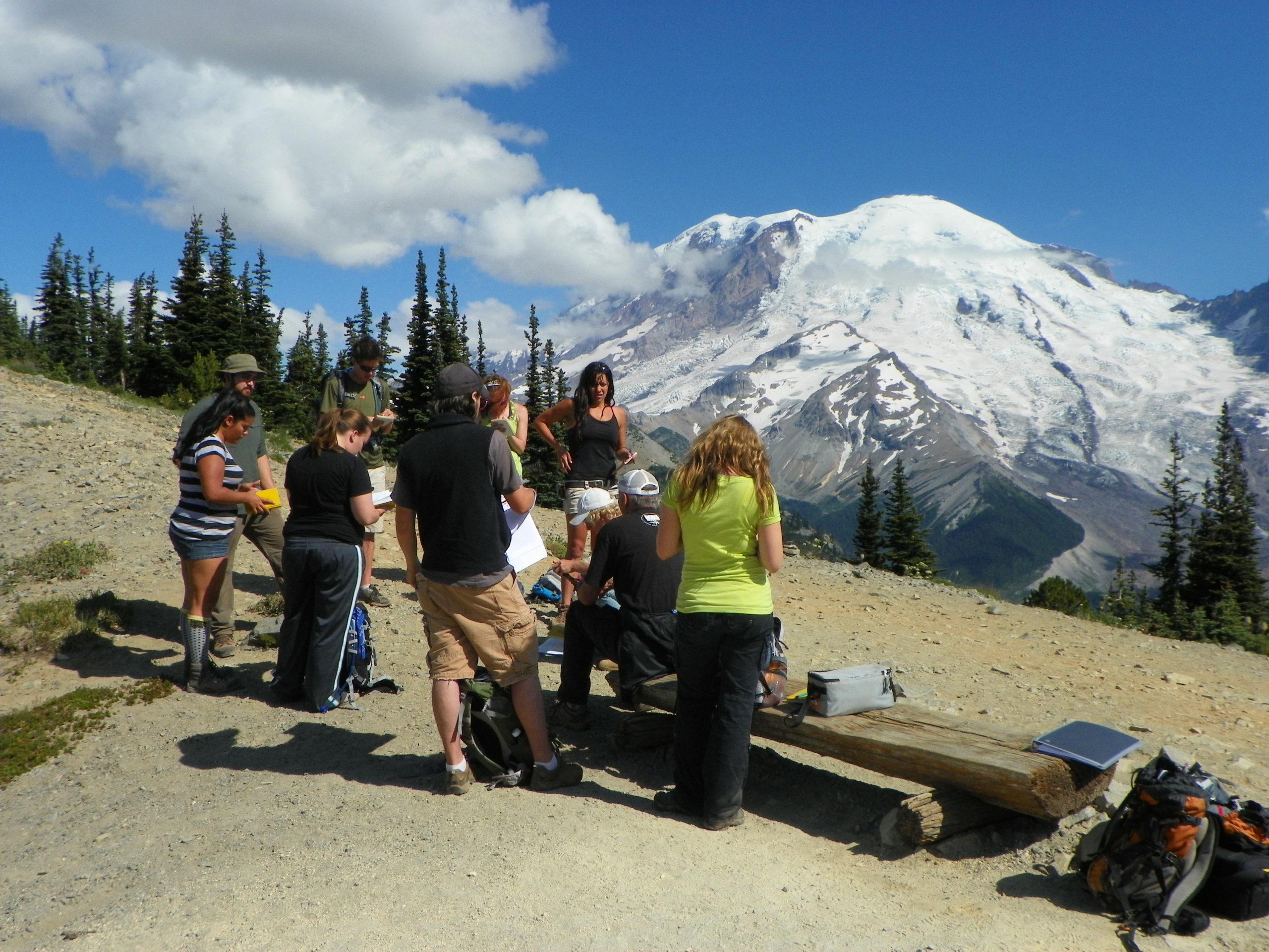 students huddled around an instructor with a snow capped mountain in the distance