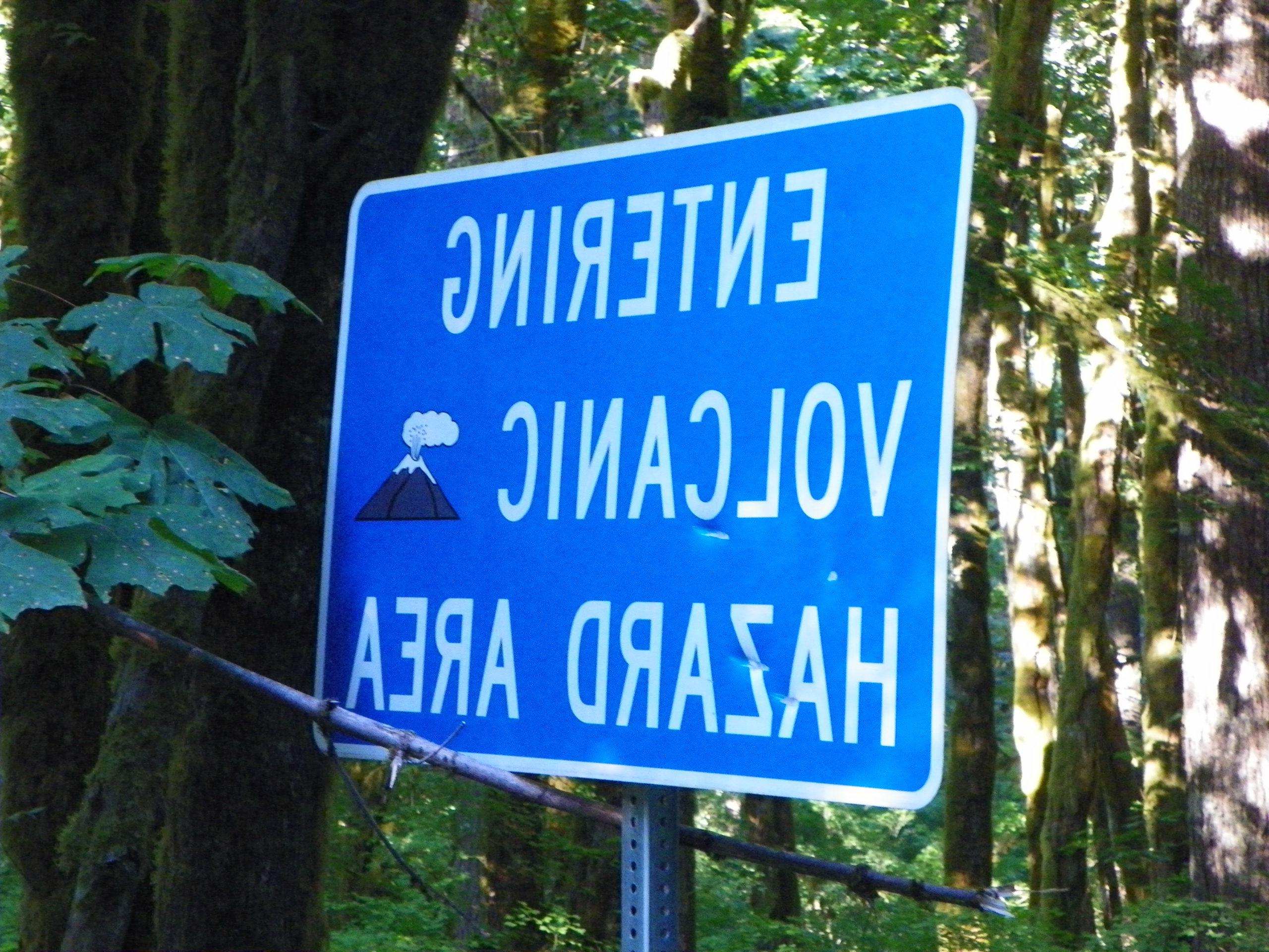 blue sign with a smoking volcano cartoon with the text entering volcanic hazard area